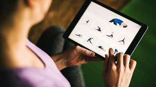 En kvinde sidder med Yoga Studio: Mind & Body, der viser forskellige yoga-positioner på sin tablet