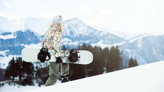 Woman climbing up hill with snowboard
