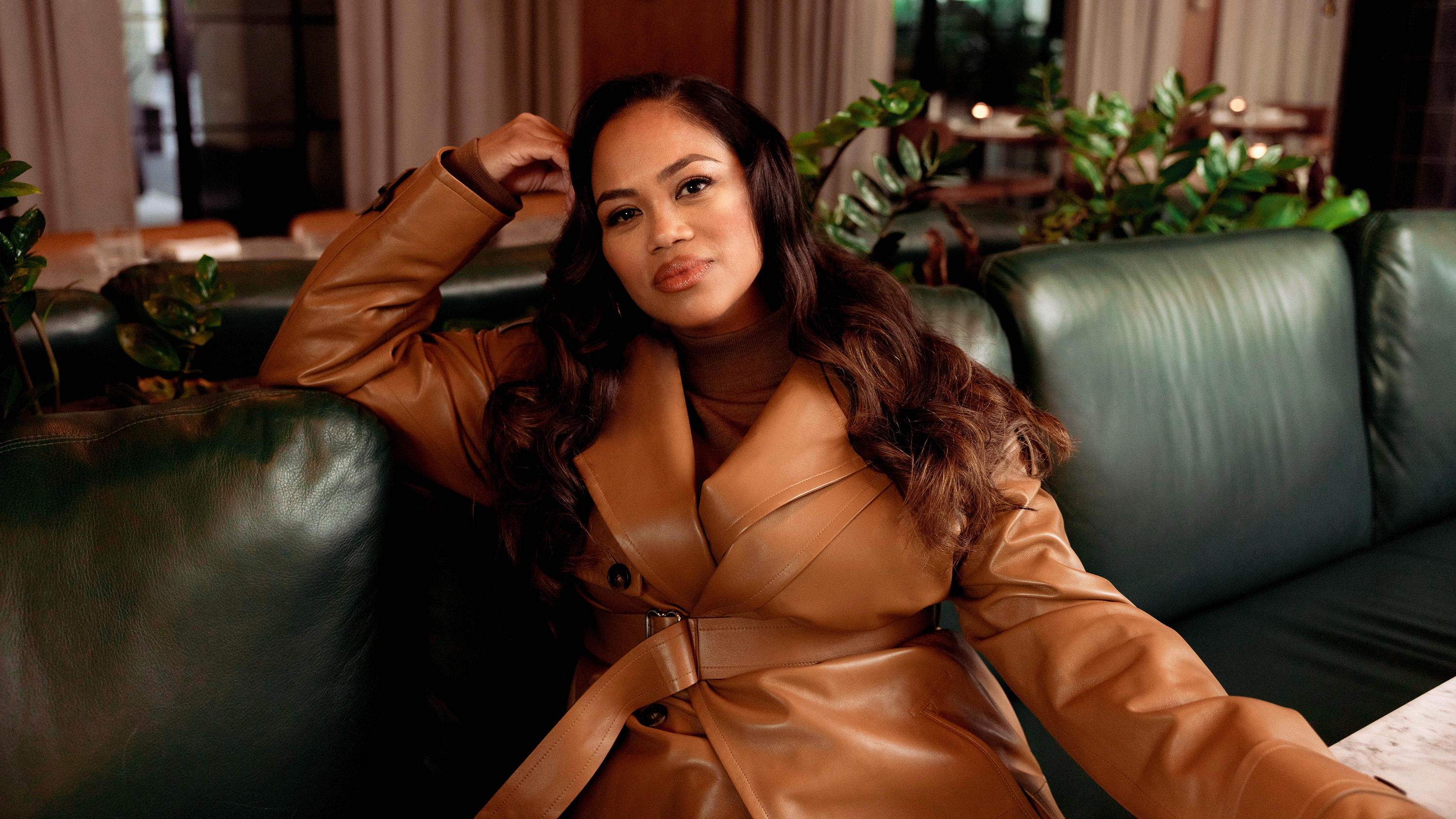 Zinzi Coogler wearing a camel leather jacket on a leather sofa