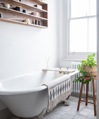 small white bathroom with freestanding cast iron bath and wooden wall storage