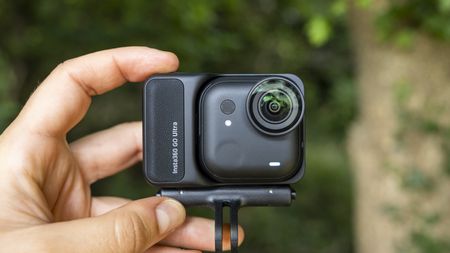 The Insta360 GO Ultra camera held by a female photographer against a green wooded backdrop