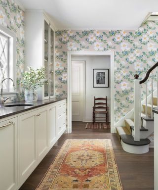 utility kitchen with patterned rug white cabinets and staircase with floral wallpaper