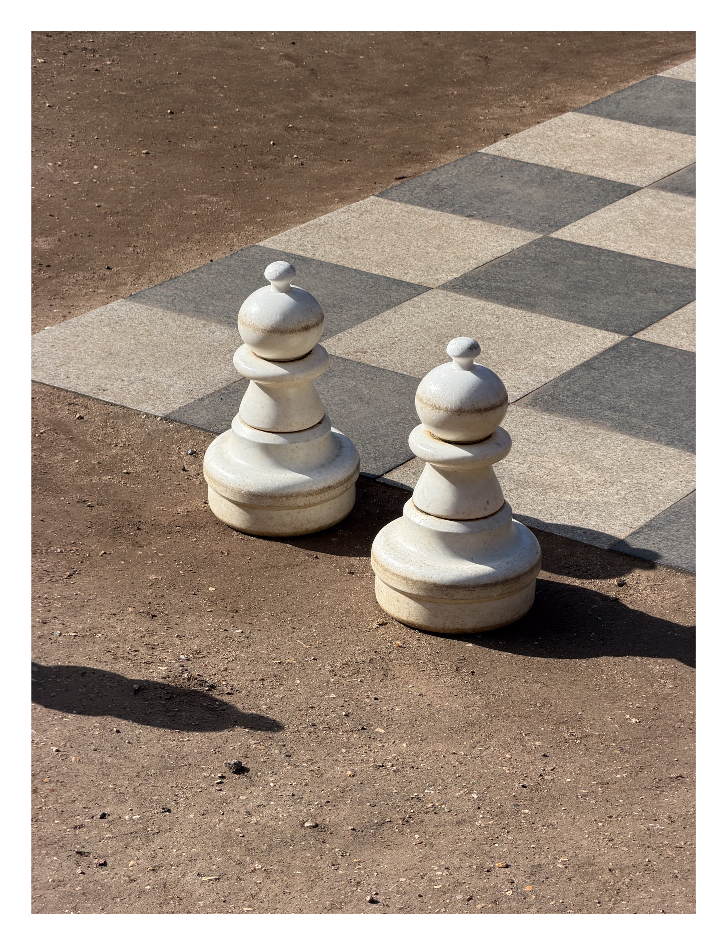 Two oversided pawns from a game of chess in the sun next to a chess board