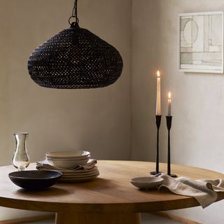 A dining table with black metal candlesticks, a low pendant light and crockery