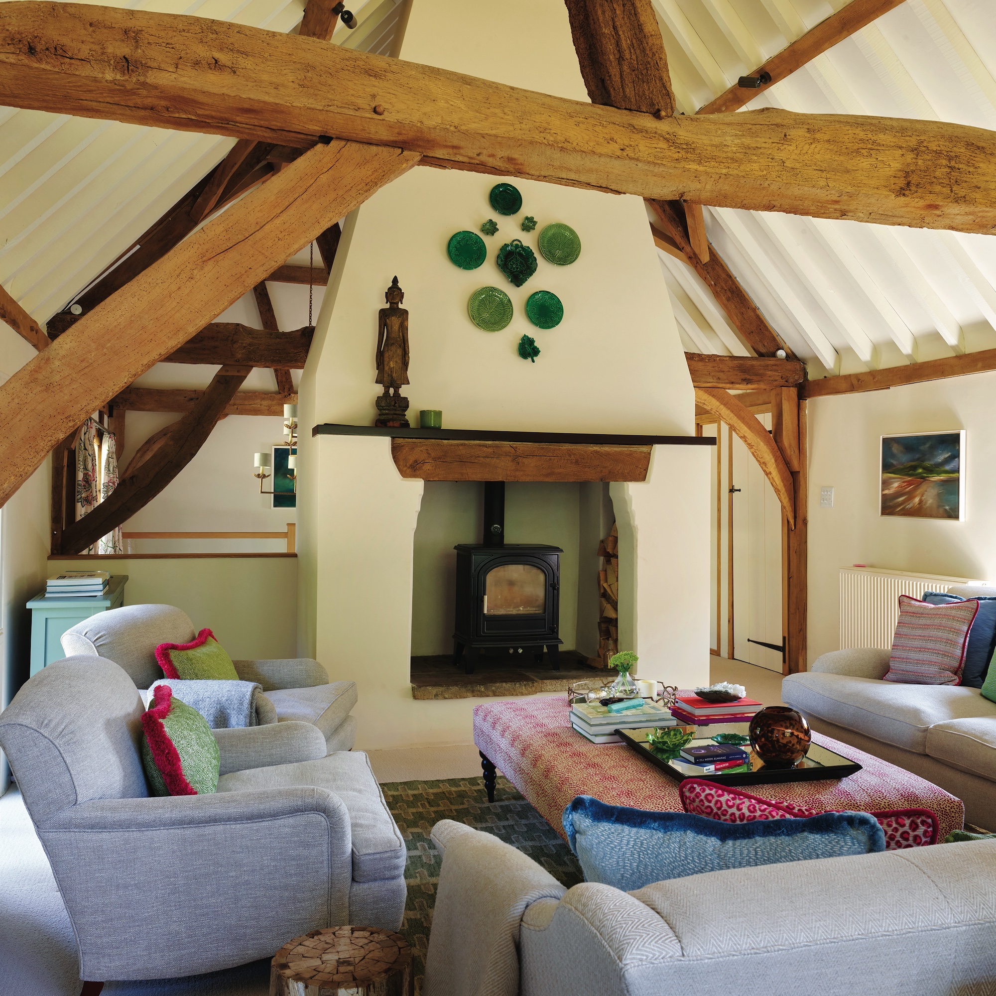 seating area in barn conversion showing vaulted beamed ceiling and arrangement of sofas and chairs around fireplace and woodburning stove