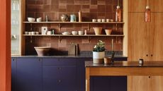 Pluck kitchen with terracotta tiled backsplash, timber cabinets, open shelving, purple cabinets, orange column, and freestanding kitchen island