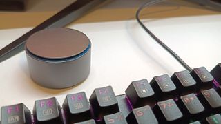 A remote control dial for a Quntis lightbar sitting behind a keyboard on a white desk