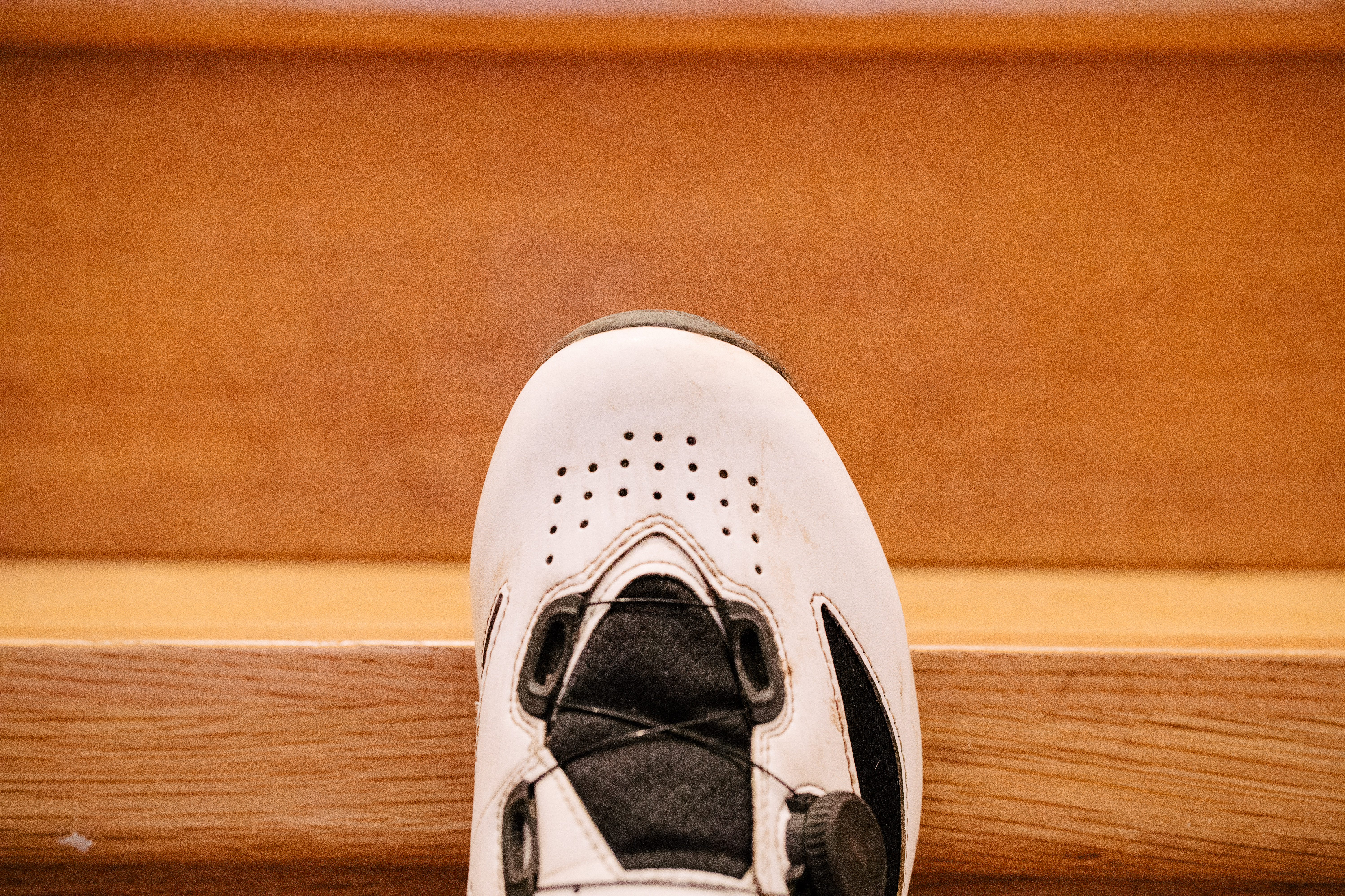 A white gravel bike shoe on wooden stairs