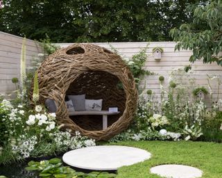 A small urban wildlife bird friendly garden chamomile lawn stepping stones and a woven willow pod with bench and cushions
