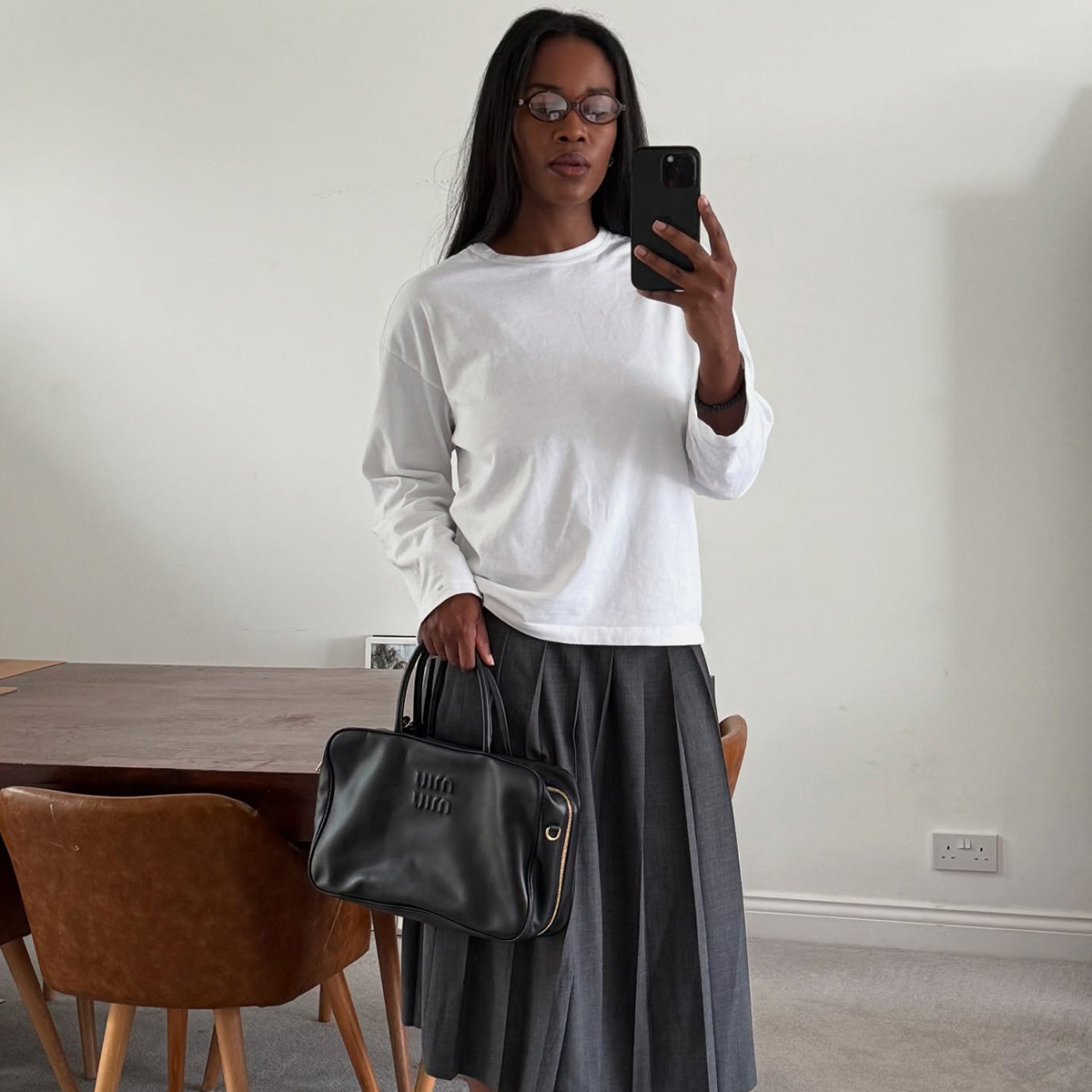 Marilyn wears a white long-sleeve shirt, pleated skirt, and miu miu bag.