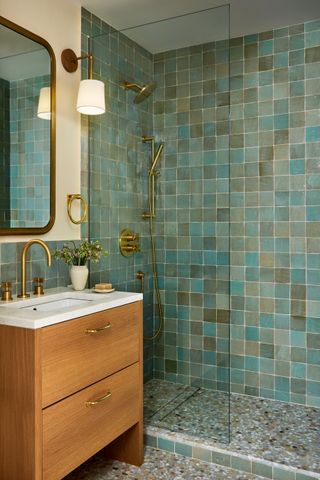 a bathroom with green zellige tiles and a wooden vanity