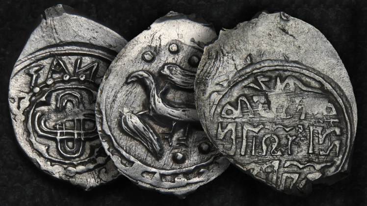 three stamped silver coins slightly overlapping one another against a black background