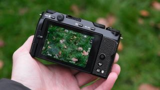 Fujifilm X-M5 camera from behind held in a hand with an image of grass with some brown leaves on the screen