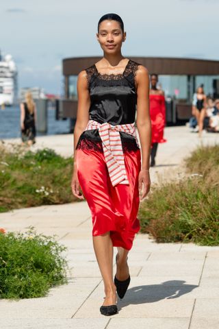 a model wears a black tank top and red skirt with a striped sweater around her waist