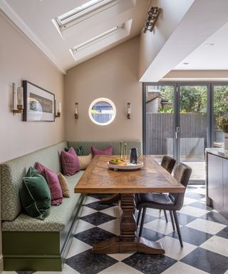 dining area with soft pink walls, an olive green bench seat and a wooden dining table with a monochrome checkerboard floor