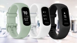 Three Garmin Vivosmart 5 fitness trackers in mint, white, and black, on top of a blurred gym background