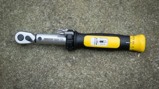 A black and yellow Pedros torque wrench lays on a paved floor