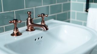 bronze taps on a white sink with green subway tiles beyond