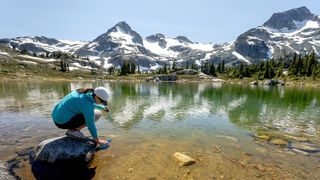 Hiker collecting water from glacial lake