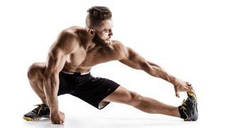 Best hamstring exercises: Man on a white background performing a hamstring stretch with left leg and arm extended