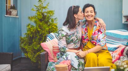 A mother and daughter in colorful clothes sit happily outside. 