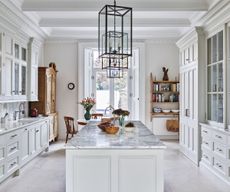 White kitchen with built-in cabinets and drawers, marble island and vintage wood furniture