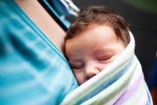 A mom swaddles her baby close to her in a blanket.