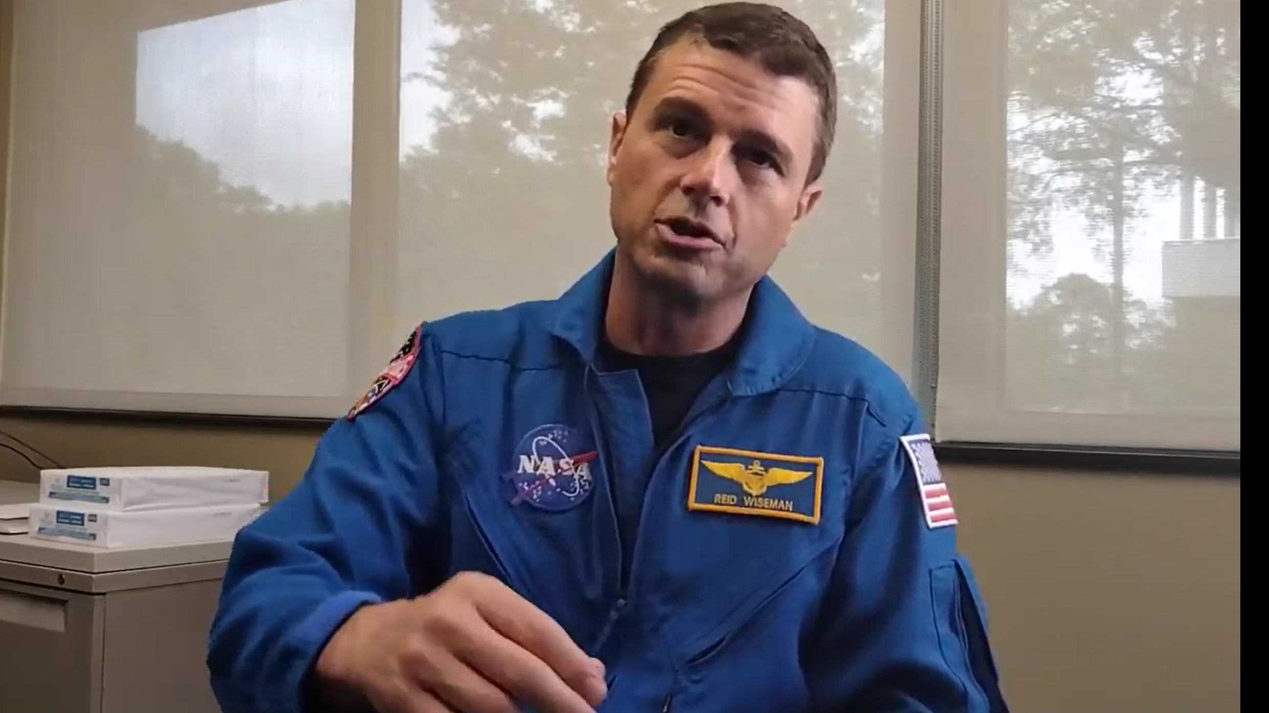 nasa astronaut reid wiseman in his flight suit talking to the camera. nasa's path is on his chest along with his name tag