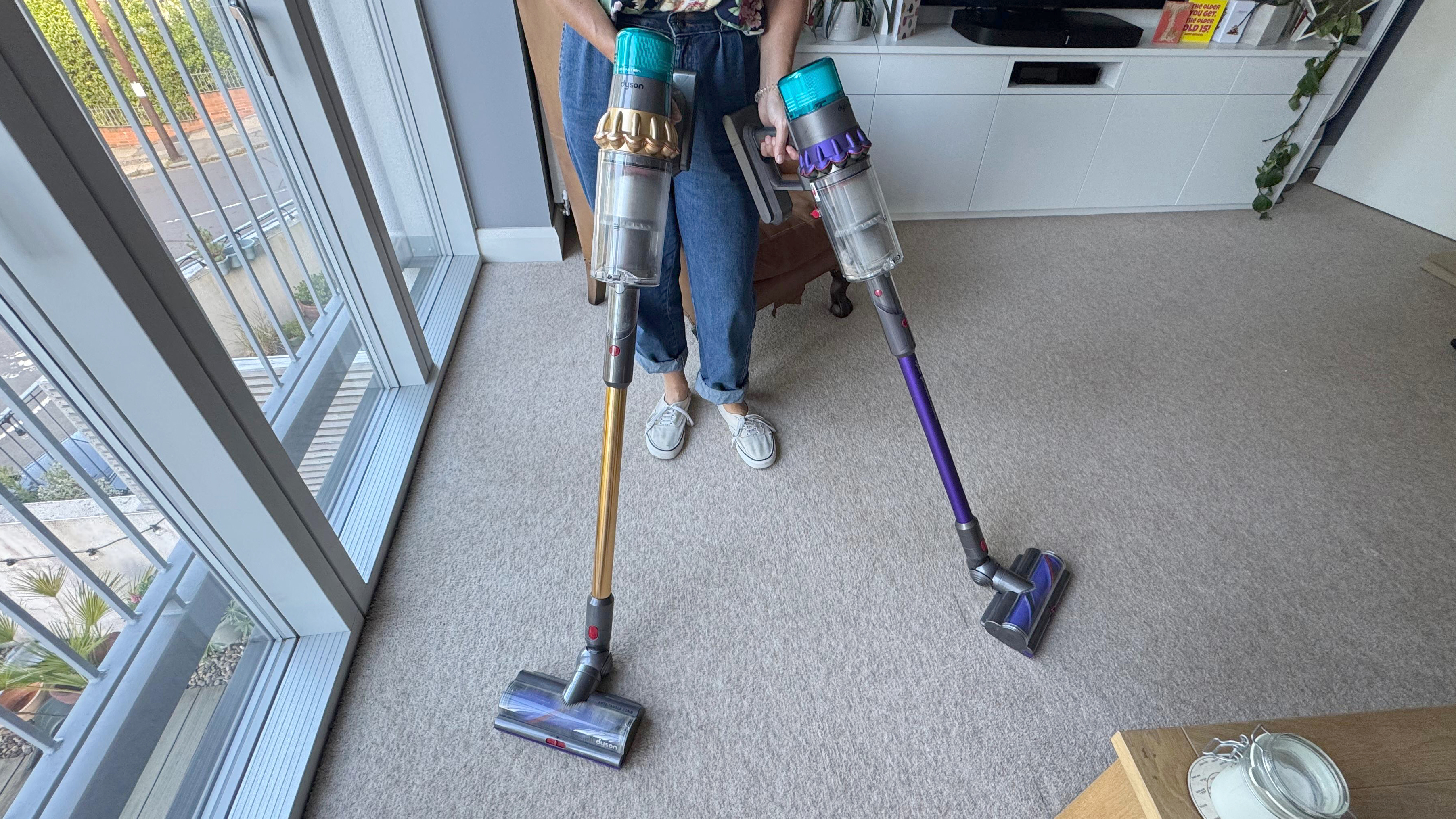 Author holding Dyson V15 Detect and Gen5detect vacuum cleaners in a carpeted living room