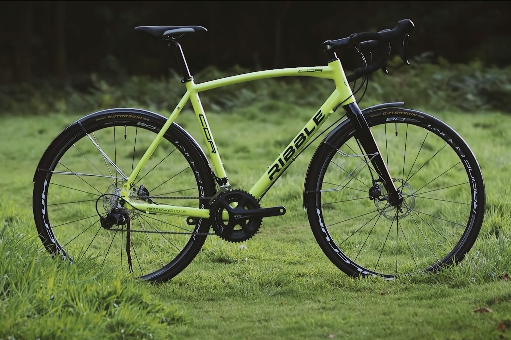 A bright yellow Ribble bike with external cables and mud guards in a field