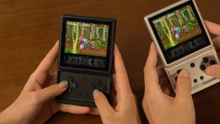 Two sets of hands holding Anbernic RG Rotate, with black version on left and silver on right.