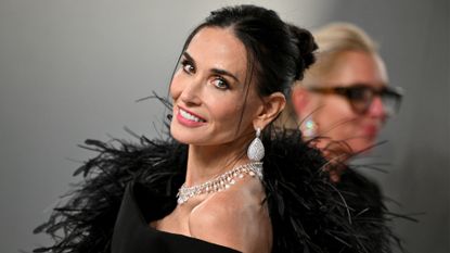 Image of Demi Moore looking over her should and smiling with her black hair in an updo and wearing a black feather gown