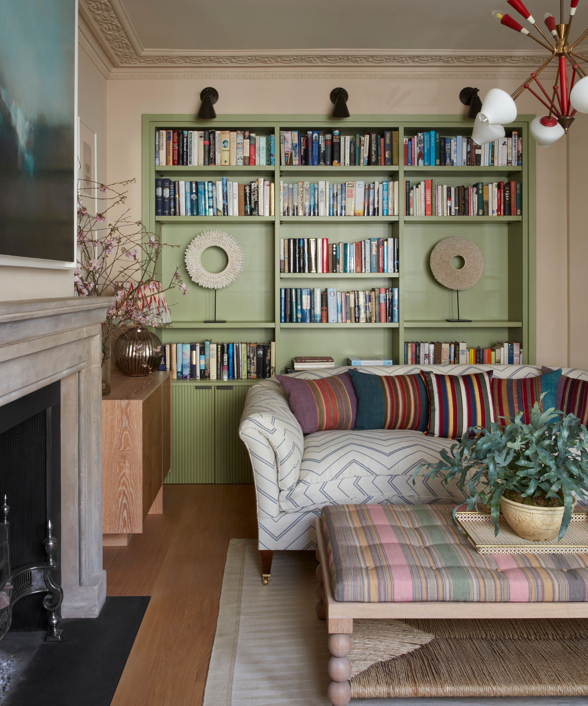 Neutral living room with pale green built in shelving, a stone fireplace, patterned cream couch and striped ottoman