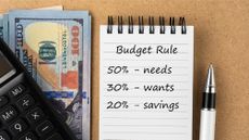 A notepad with 50-30-20 budgeting rules on it next to a calculator and cash. 
