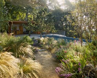 Naturalistic planting beds flanking a path leading up to a pool house and pool