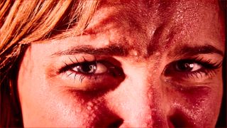 Close up of a young blonde woman, covered in perspiration, frowning, tense and nervous - tinted red.