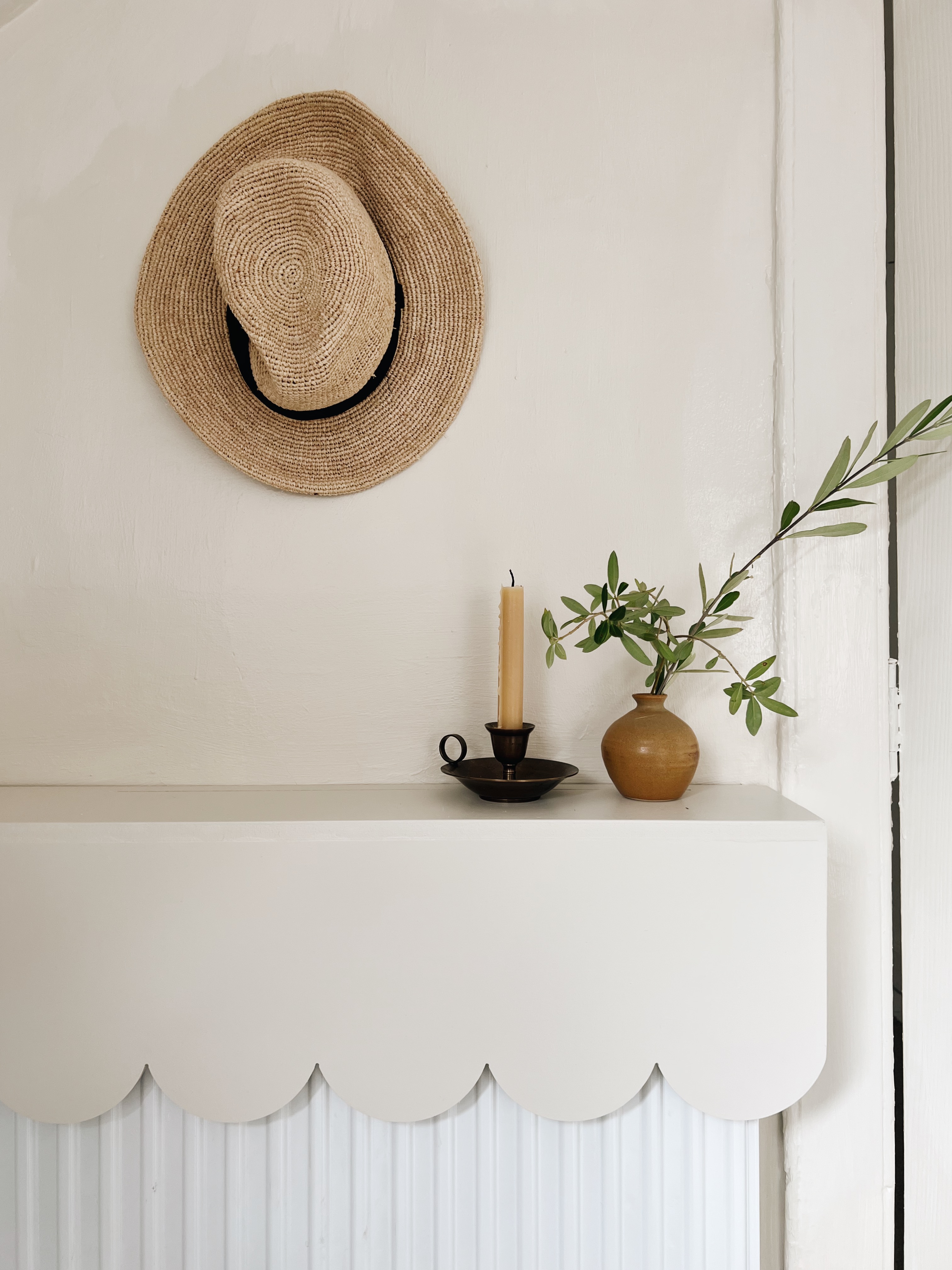 a scalloped edge radiator cover in neutral tones with a small vase and candle resting on the surface
