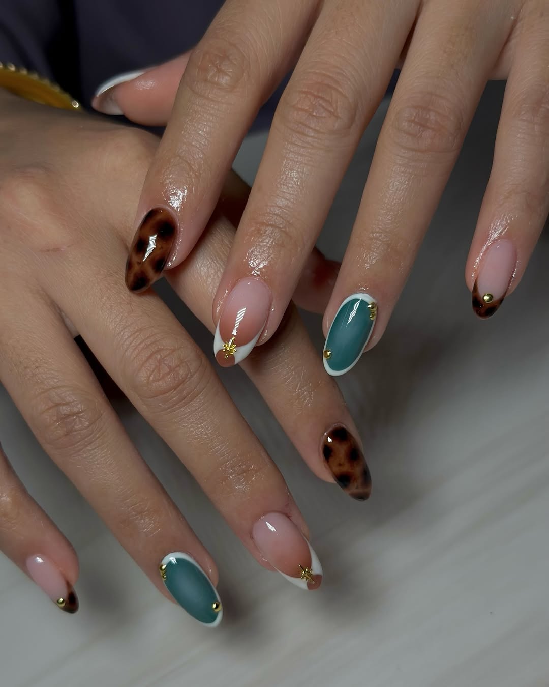 Close-up photo of a person&amp;rsquo;s hands showcasing brown tortiseshell prints, white French tips, and blue ovals painted on almond nails.
