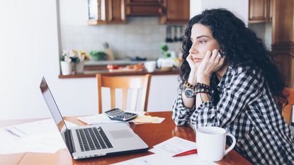 A divorcing woman looks thoughtful as she looks at her laptop at her kitchen table.