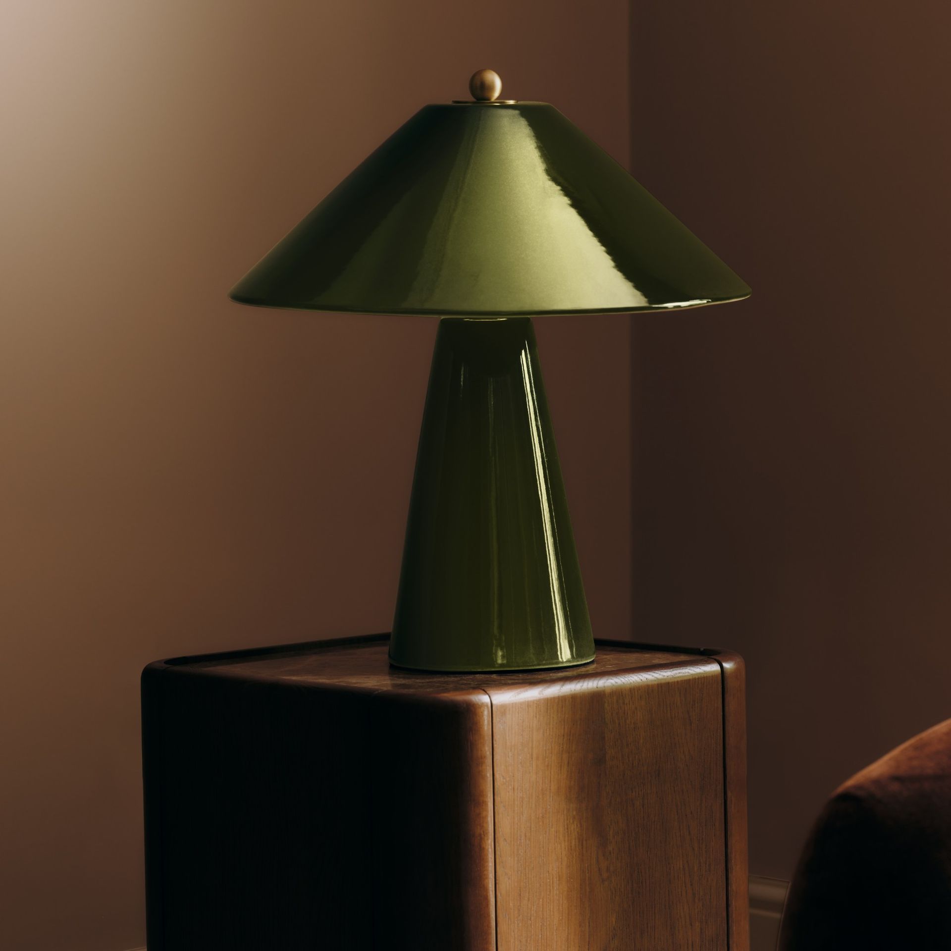 M&S All Over Ceramic Table Lamp in green on a dark wood side table next to a brown velvet sofa set against brown-painted walls