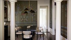 A white dining room with framed wallpapers, a black table, white armchairs with gold accents, a pendant lamp and a rug