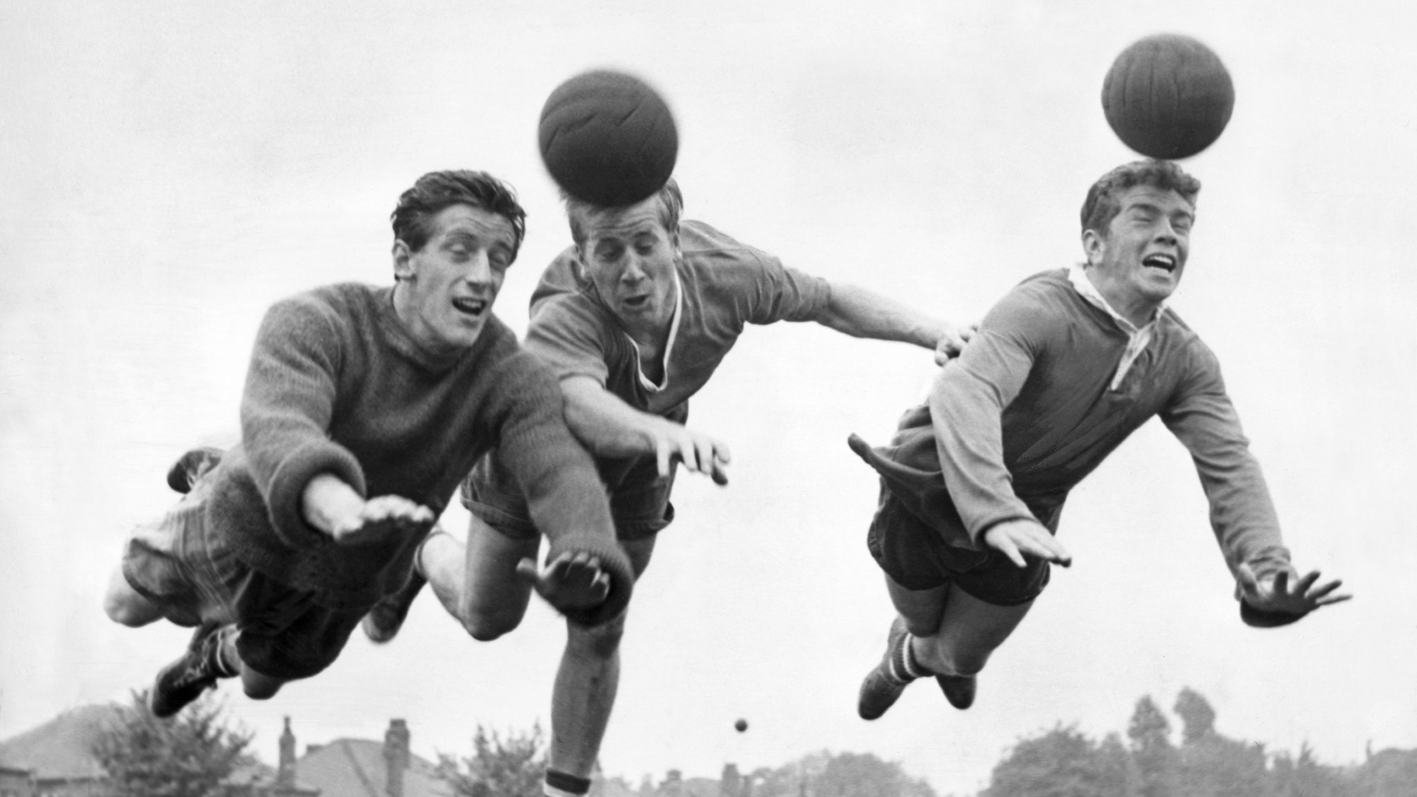 Three 1960s footballers diving to head a football