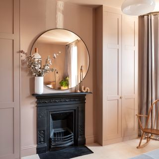 A bedroom colour-drenched in a beige shade with a pink undertone and a black fireplace