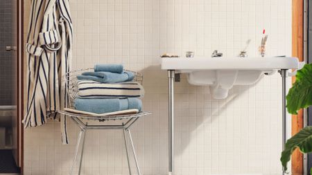 Retro-style bathroom featuring white ceramic tiles and a mid-century inspired chrome chair, which is holding a stack of fluffy bath towels. A coordinating robe hangs alongside.