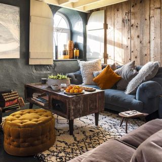 Living area with two velvet sofas and mustard coloured Ottoman around rustic wooden coffee table.