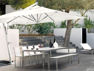 Tribu Vitino Pendulum Tilt Garden Parasol in a large outdoor patio area with dining table and bench