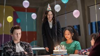 Ms. Sigsby in birthday hat while Kalisha stares at candles on cake during party in The Institute