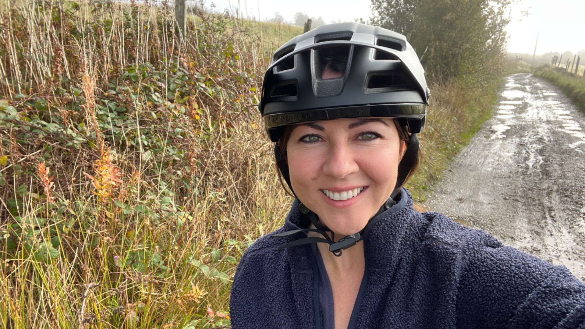 Susan Griffin mountain biking down muddy and gravel path in the Pennines, smiling and wearing a helmet