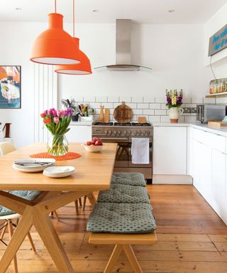 White kitchen with kitchen table and benches and orange pendants