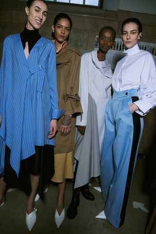 Models wear asymmetrical dresses, trench, wide legged trousers, pointed mules and shirts